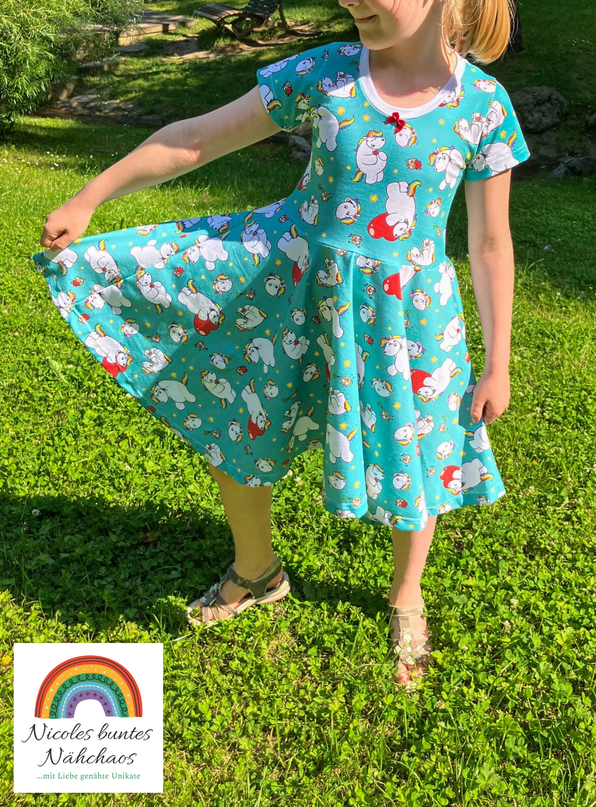 Mädchen trägt das Drehkleid "Marlene" mit dem Design "Pummel und Norbert Türkis" mit kurzen Ärmeln. Sie hält den Rock an der Seite hoch, um den Tellerrock zu präsentieren. Weißes Bündchen am Rundhalsausschnitt, kleine rote Schleife zur Verzierung.