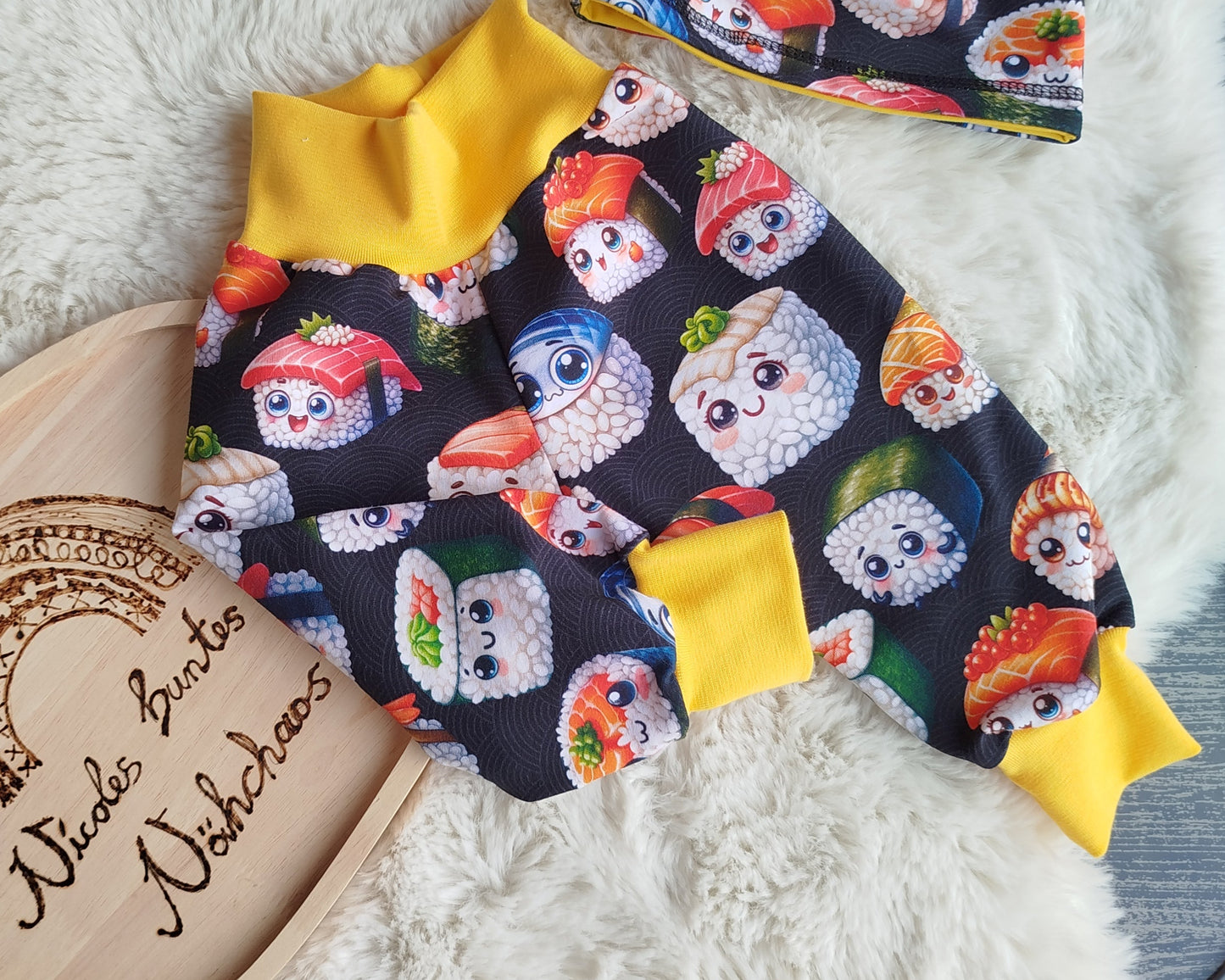 Beispielbild einer Pumphose. Gelbes Bündchen am Bauch und an den Beinen. Muster der Pumphose: schwarzer Hintergrund mit unterschiedlichen lächelnden Comicartigen Sushis.