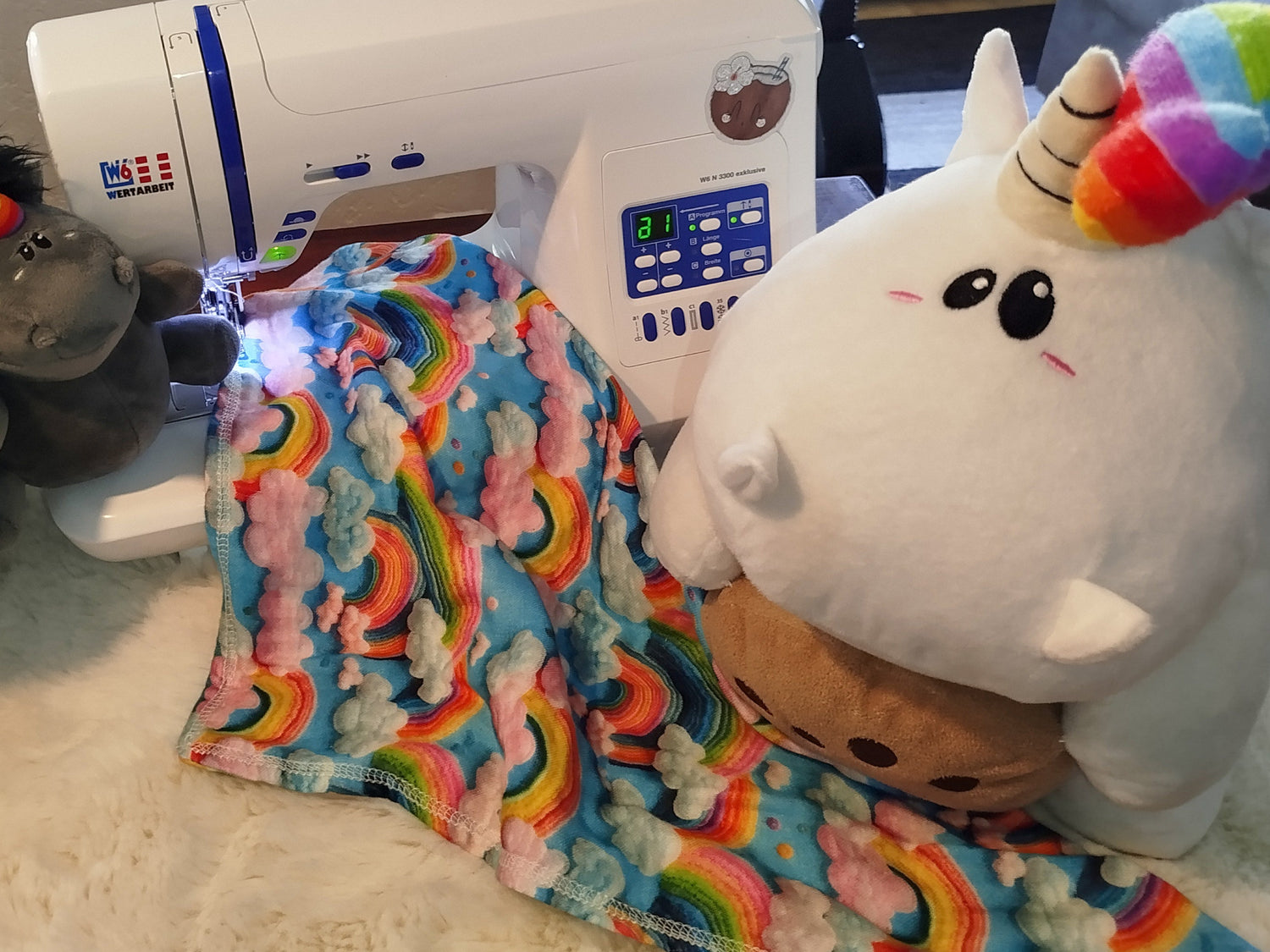 Gurmmeleinhorn und Pummeleinhorn sitzen um die Nähmaschine herum, zwischen ihnen liegt ein Tuch. Symbolbild für die Kategorie Pummeleinhorn.