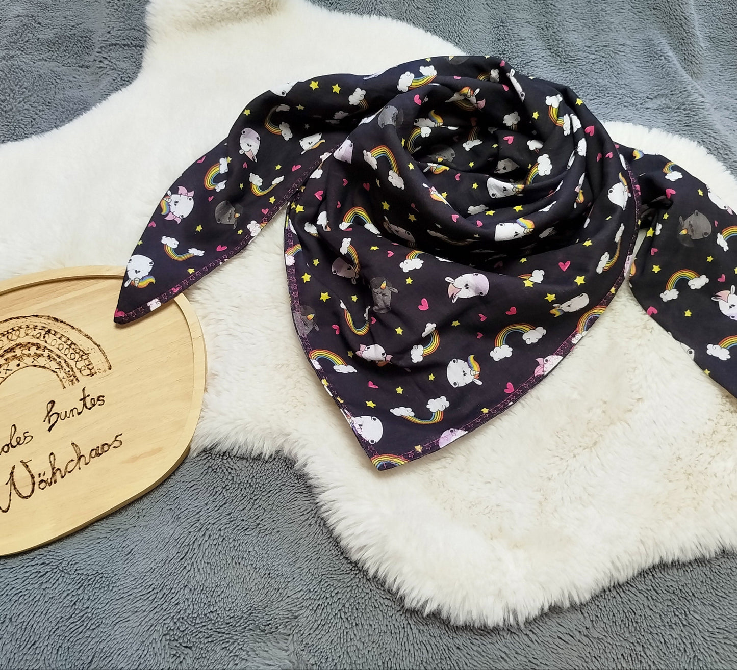Flatlay eines doppeltgenähten XL Dreiecktuchs für Erwachsene aus Musselin mit Design "Glitzerweltler schwarz. Tuch liegt auf einem weißen Kunstfell.