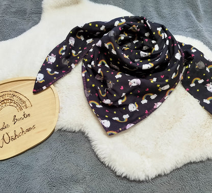 Flatlay eines doppeltgenähten XL Dreiecktuchs für Erwachsene aus Musselin mit Design "Glitzerweltler schwarz. Tuch liegt auf einem weißen Kunstfell.